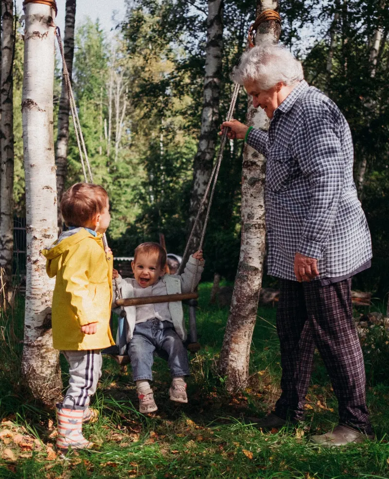 A grandfather pushing his grandchildren on a swing in the garden