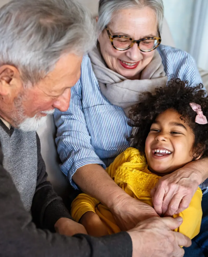 Grandparents hugging their laughing granddaughter on the sofa